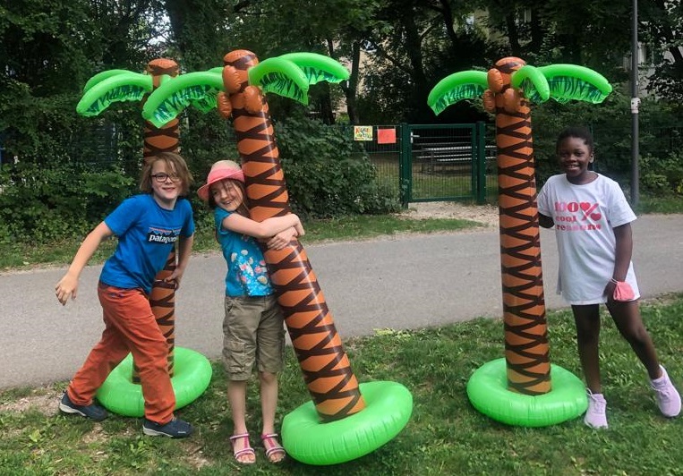 Drei Kinder die im Park an aufblasbaren Palmen stehen